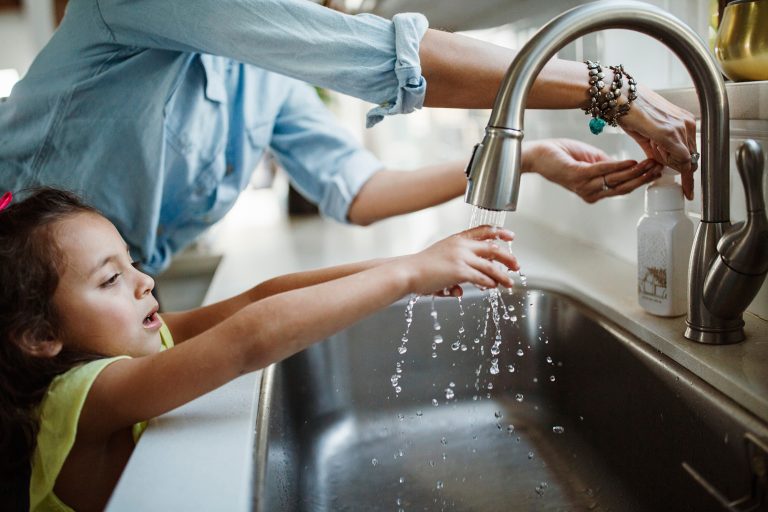 Child washing hands next to parent